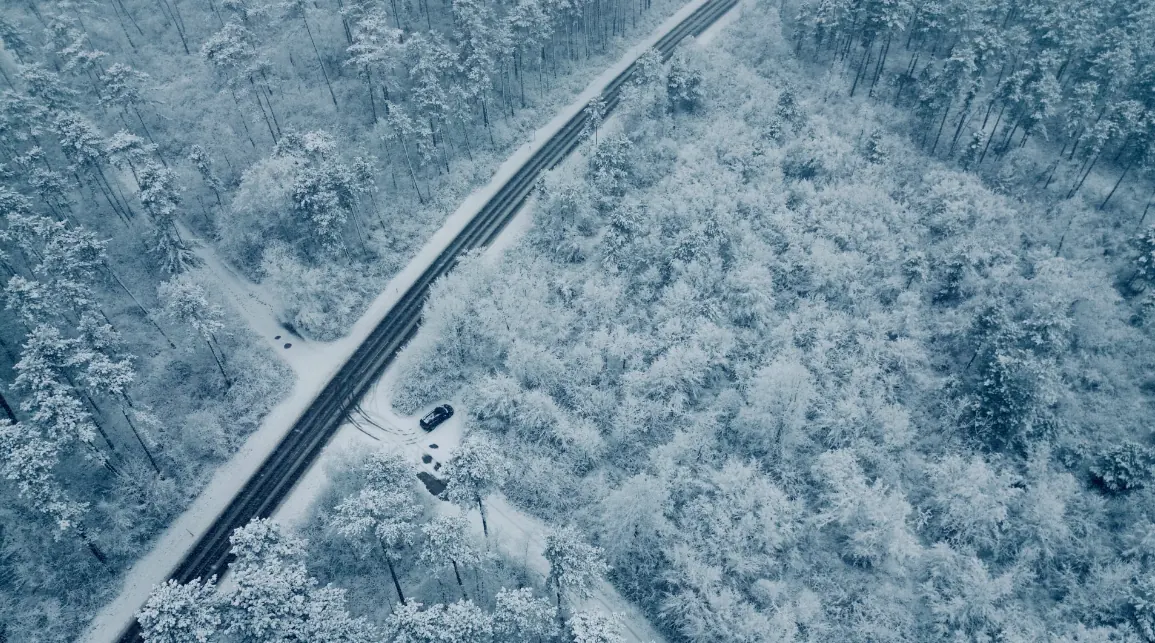 Drohnenaufnahme einer verschneiten Waldstraße